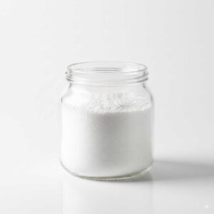 پودر سفید کربنات سدیم (سودا اش) در ظرف شیشه‌ای روی زمینه سفید
